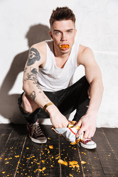 Tattooed man with popato chips falling out from his mouth