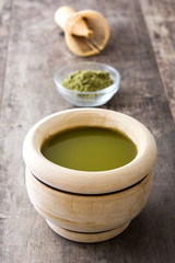 Matcha green tea in a bowl and bamboo whisk, on wooden background
