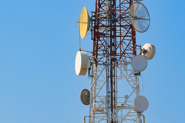 Mobile phone communication antenna tower with satellite dish on blue sky background