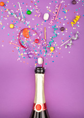 Colorful party attributes fly out from botle of champagne wine. on a lilac background. Flat lie. Celebrate concept. High resolution photo.