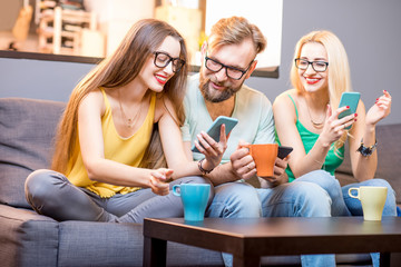 Young friends sitting with smart phones on the couch at home