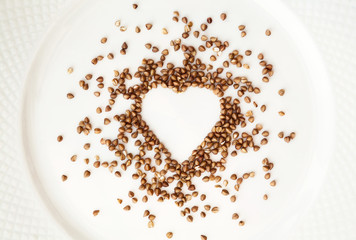 Buckwheat in a shape of heart spilled on a plate. Raw food ingredient background. Love for cooking concept