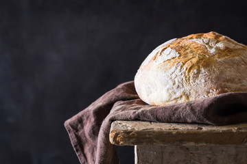 Homemade bread loaf on old table. Dark background