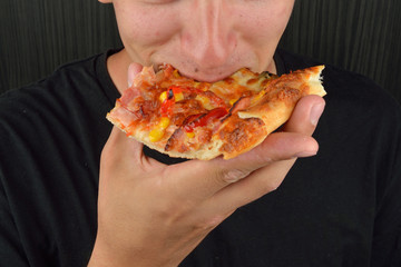 Portrait of a greedy young man eating pizza on a dark background. Fast food, unhealthy