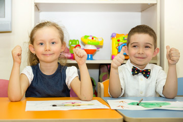 Adorable children boy and girl draws a brush and paints in nursery room. Kid in kindergarten in Montessori preschool class.