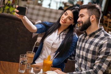 Couple taking selfie with camera phone in cafe