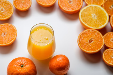 A glass of juice and cut oranges and tangerines on a white background