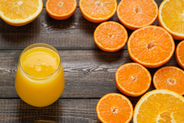 A glass of juice and cut oranges and mandarins on the wooden background