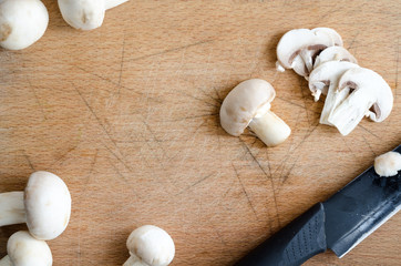 Champignon mushrooms and a knife on a wooden cutting board - top view