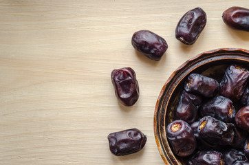 Fresh dates in a wooden bowl and more dates on a table around the bowl - top view