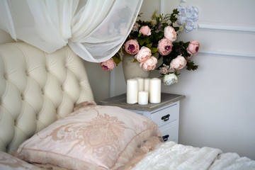 Ваза с цветами, свечи стоят на тумбочке рядом с кроватью в спальне

