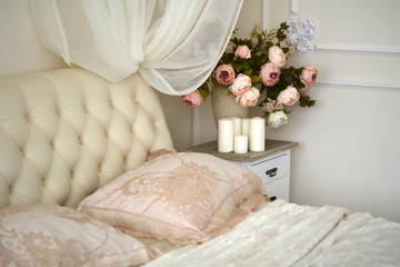 Ваза с цветами, свечи стоят на тумбочке рядом с кроватью в спальне

