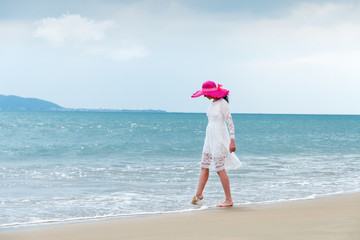 Girl in white dress and hat touches sea water