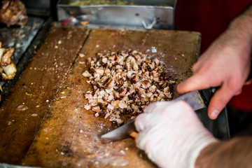Man is preparing kokorec (fried sheep bowel) with knife on wooden surface.