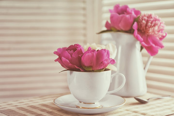 Bouquet of beautiful flowers in cup and vase on table