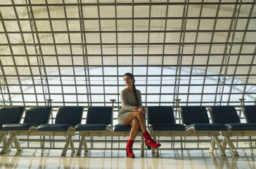 Beautiful young woman is sitting on the bench in an airport and waiting a flight