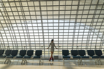 Beautiful young woman is standing in the airport, waiting a flight and looking at window of travel lounge