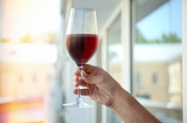 Male hand holding glass of red wine on window background