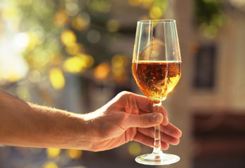 Male hand holding glass with wine on blurred natural background
