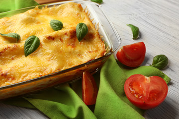 Traditional lasagna in glass baking dish, tomatoes and napkin on table