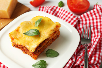 Plate with delicious lasagna and napkin on table