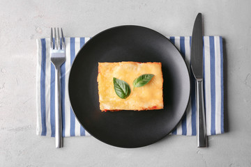 Black plate with delicious lasagna and striped napkin on table