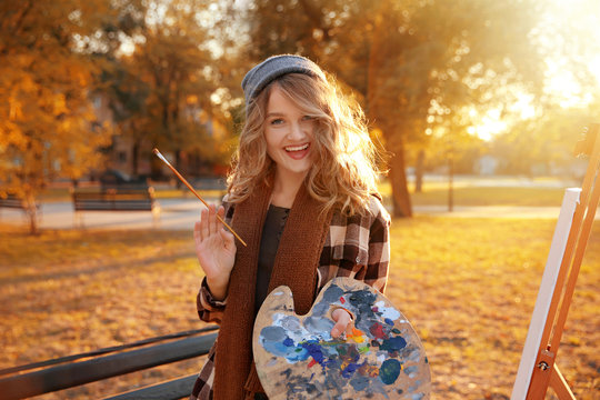 Young female artist with palette and brush in autumn park