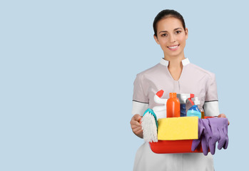 Hotel female chambermaid holding cleaning supplies on color background