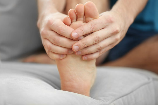 Young man suffering from podalgia at home, closeup
