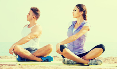 Fototapeta premium Cross-legged couple practice yoga on beach in morning