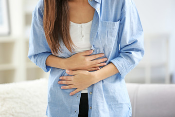 Young woman suffering from abdominal pain at home, closeup. Gynecology concept