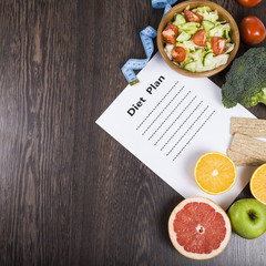 Food and sheet of paper with a diet plan on a dark wooden table.