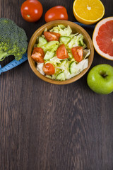 Food for diet and measuring tape on a dark wooden table.