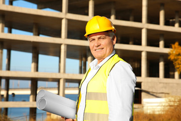 Senior engineer with drawing standing against unfinished building