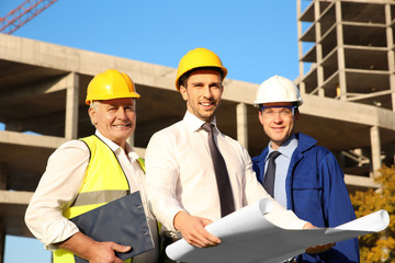 Engineer with drawing and workers standing against unfinished building