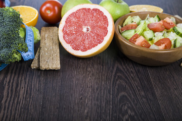 Food for diet and measuring tape on a dark wooden table.