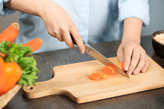 Female hands cutting carrot at table in kitchen