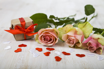 Fototapeta premium Pink roses, gift and hearts on a wooden background.
