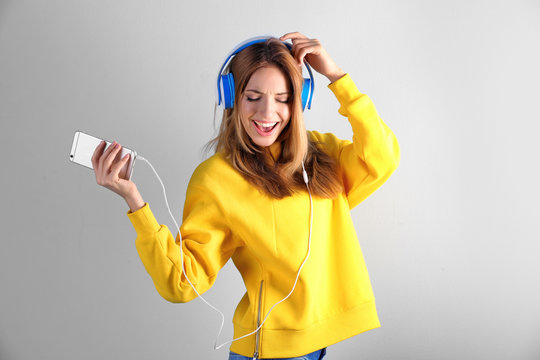 Beautiful young woman listening to music in headphones on color background