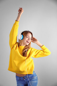 Beautiful young woman listening to music in headphones on color background