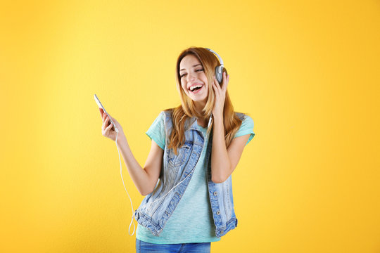 Beautiful young woman listening to music in headphones on color background