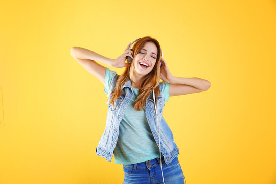 Beautiful young woman listening to music in headphones on color background
