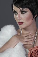 1920s style brunette dancer with short hair and jewelry. She is wearing a white hair shawl