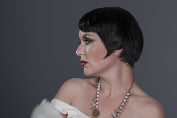 Flapper, 1920s style brunette dancer with short hair and jewelry. She is wearing a white hair shawl