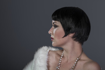 1920s style brunette dancer with short hair and jewelry. She is wearing a white hair shawl