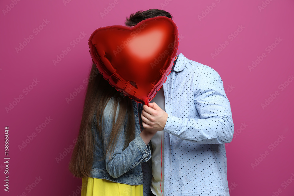 Wall mural Cute young couple with balloon in shape of heart on color background