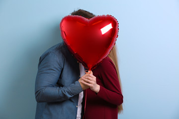 Cute young couple with balloon in shape of heart on color background