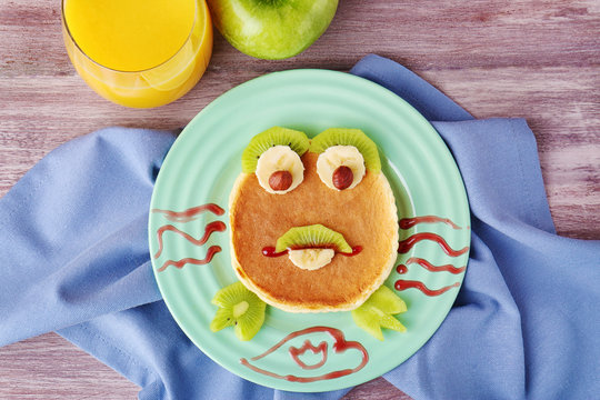 Funny pancake for kids breakfast, on wooden background