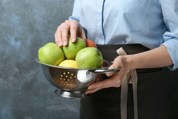 Young woman in apron holding colander with juicy apples, closeup