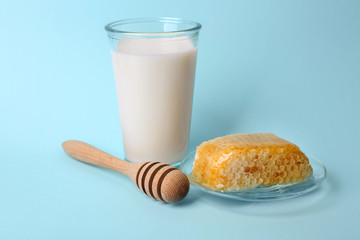 Glass of milk, honeycomb and honey dipper on blue background
